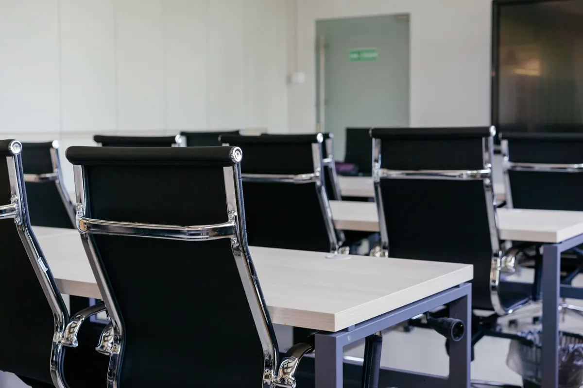 Mesa de reunião com cadeiras pretas alinhadas, em sala sóbria de negociação