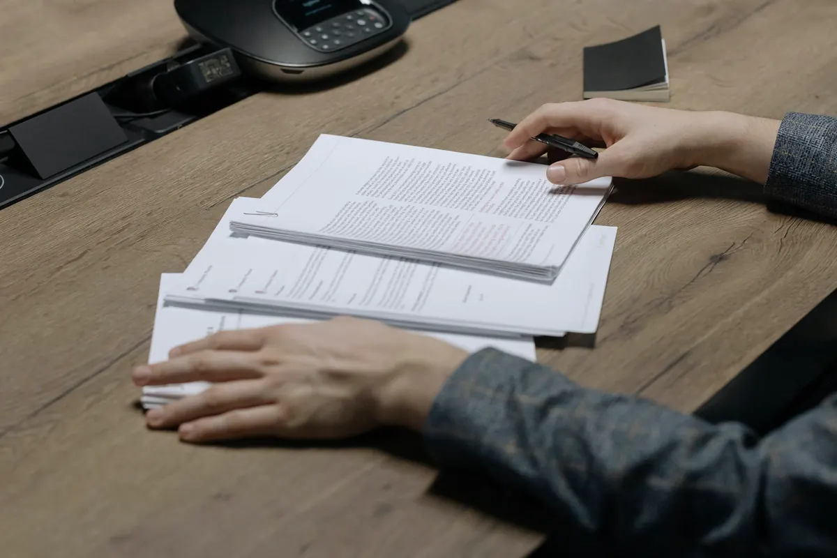 Mãos revisando um contrato impresso com anotações, sobre mesa de escritório